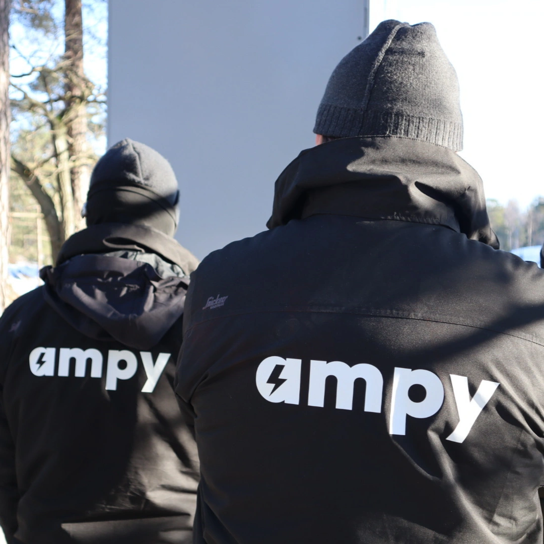 Två elektriker med Ampy-loggan synlig på ryggen som arbetar tillsammans vid en installation.